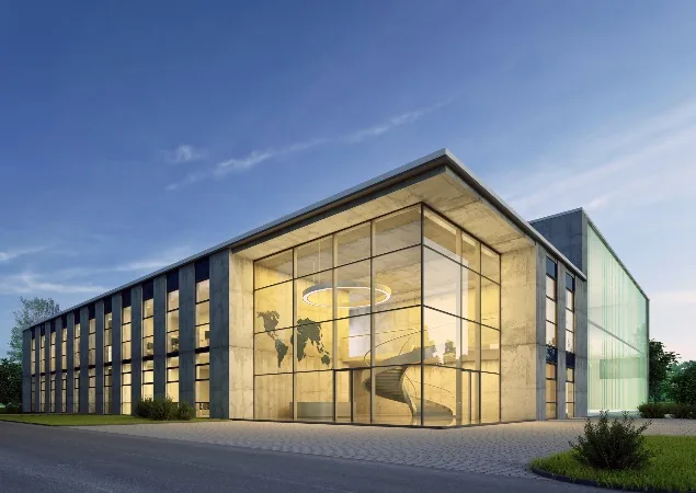 Modernes Bürogebäude mit großer Glasfassade und beleuchtetem Innenbereich bei Abenddämmerung